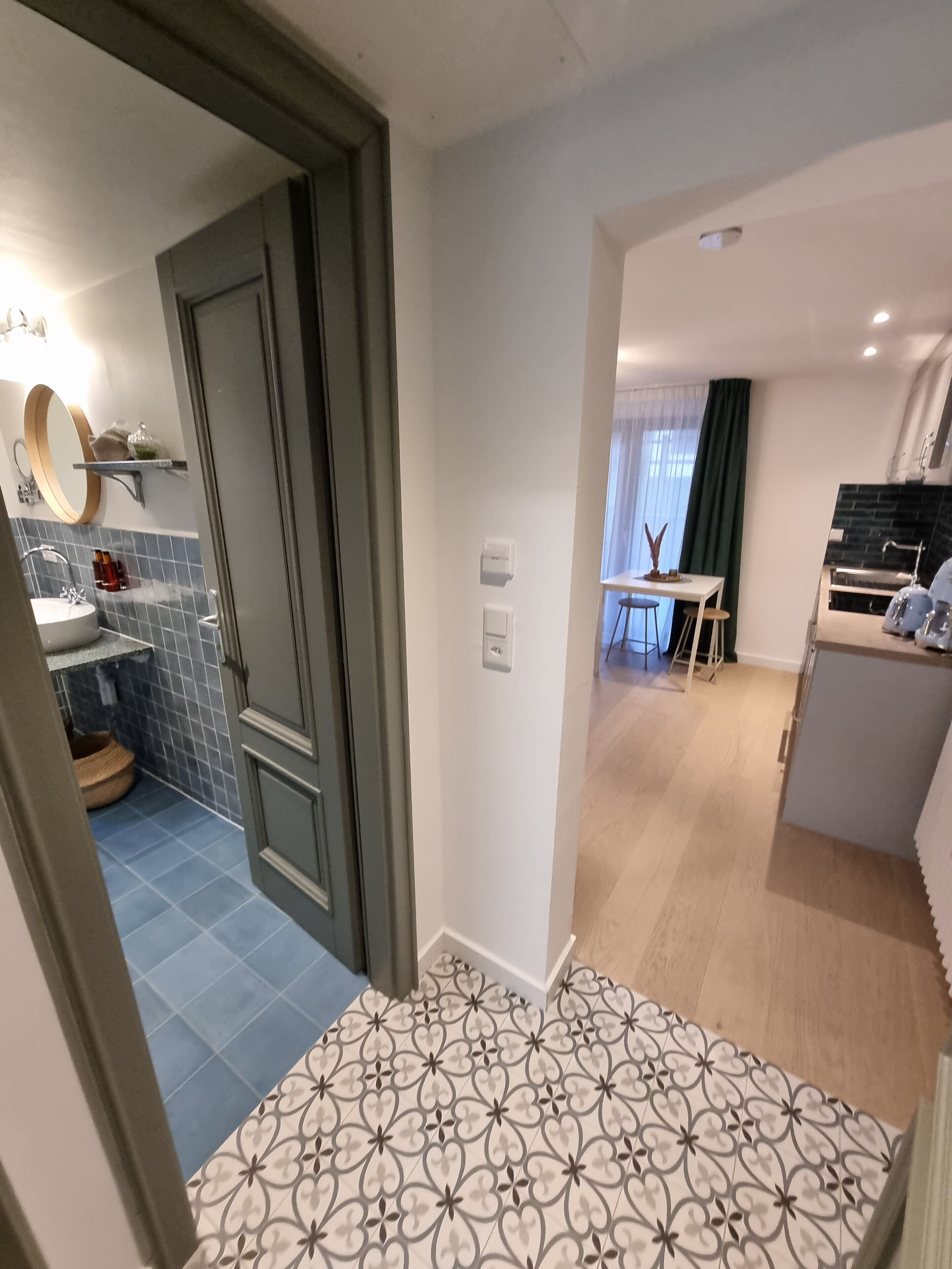 A modern kitchen with a built-in oven, a dining area with a table and chairs, and a bathroom with a sink and mirror.