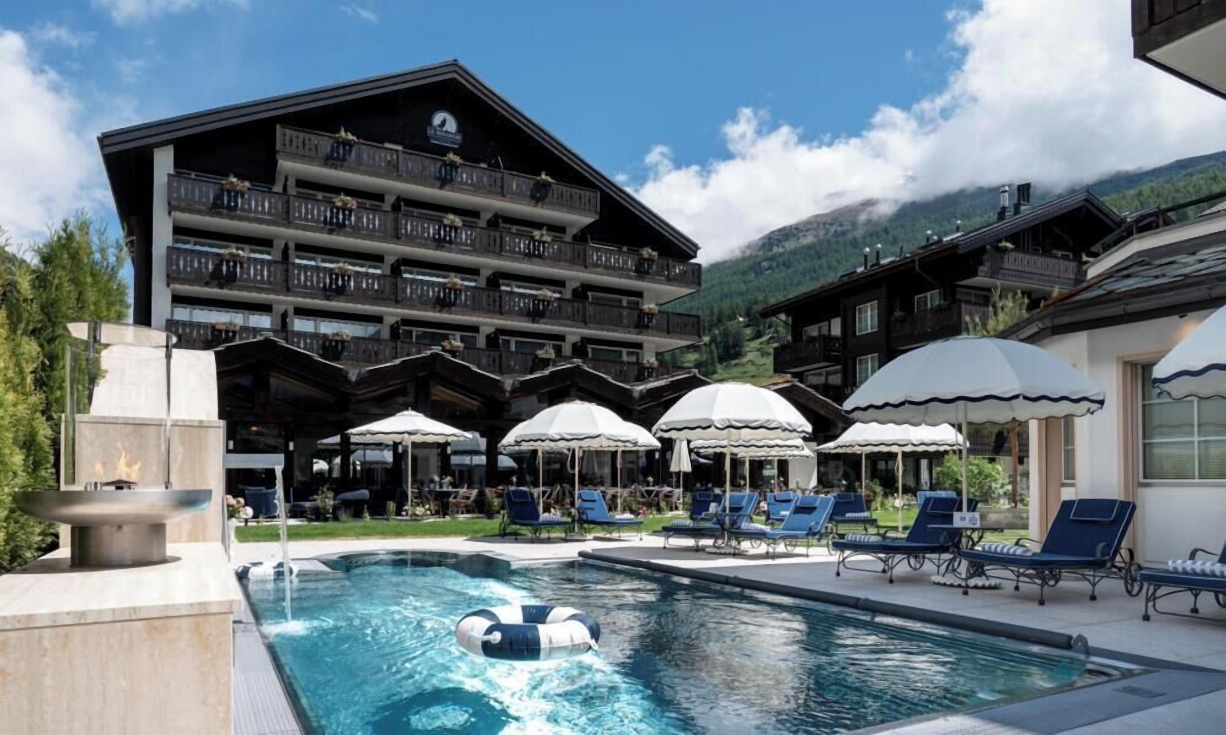 A hotel with a pool, outdoor seating, and mountain views.