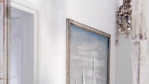 Une pièce avec un tableau représentant des voiliers au mur, une porte blanche et une petite table recouverte d’une nappe blanche.