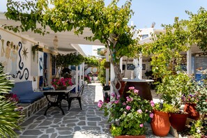 Une cour avec un sol en pierre, une table entourée de chaises, des plantes en pot et une statue.