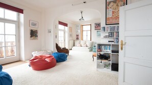 A spacious room with a white door, a bookshelf, a red bean bag, a brown chair, and a white sofa.
