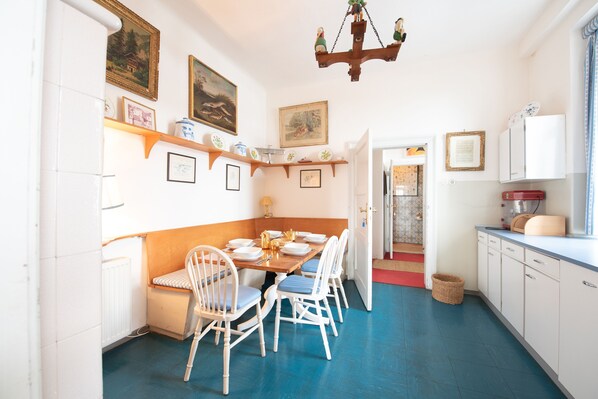 A dining area with a wooden table and white chairs, a chandelier, and wall-mounted shelves with framed pictures and decorative items.