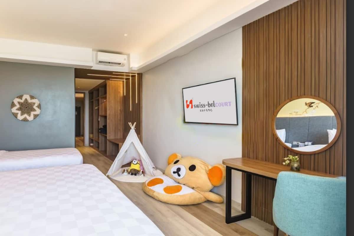 Une chambre d’hôtel avec un lit, un bureau, une chaise, un miroir, une tente décorée de peluches et un panneau encadré accroché au mur.