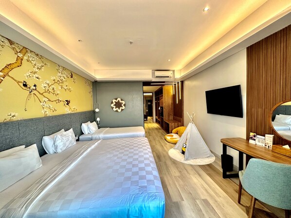 A hotel room with two beds, a wall-mounted TV, a wooden desk, and a small seating area with a tent.