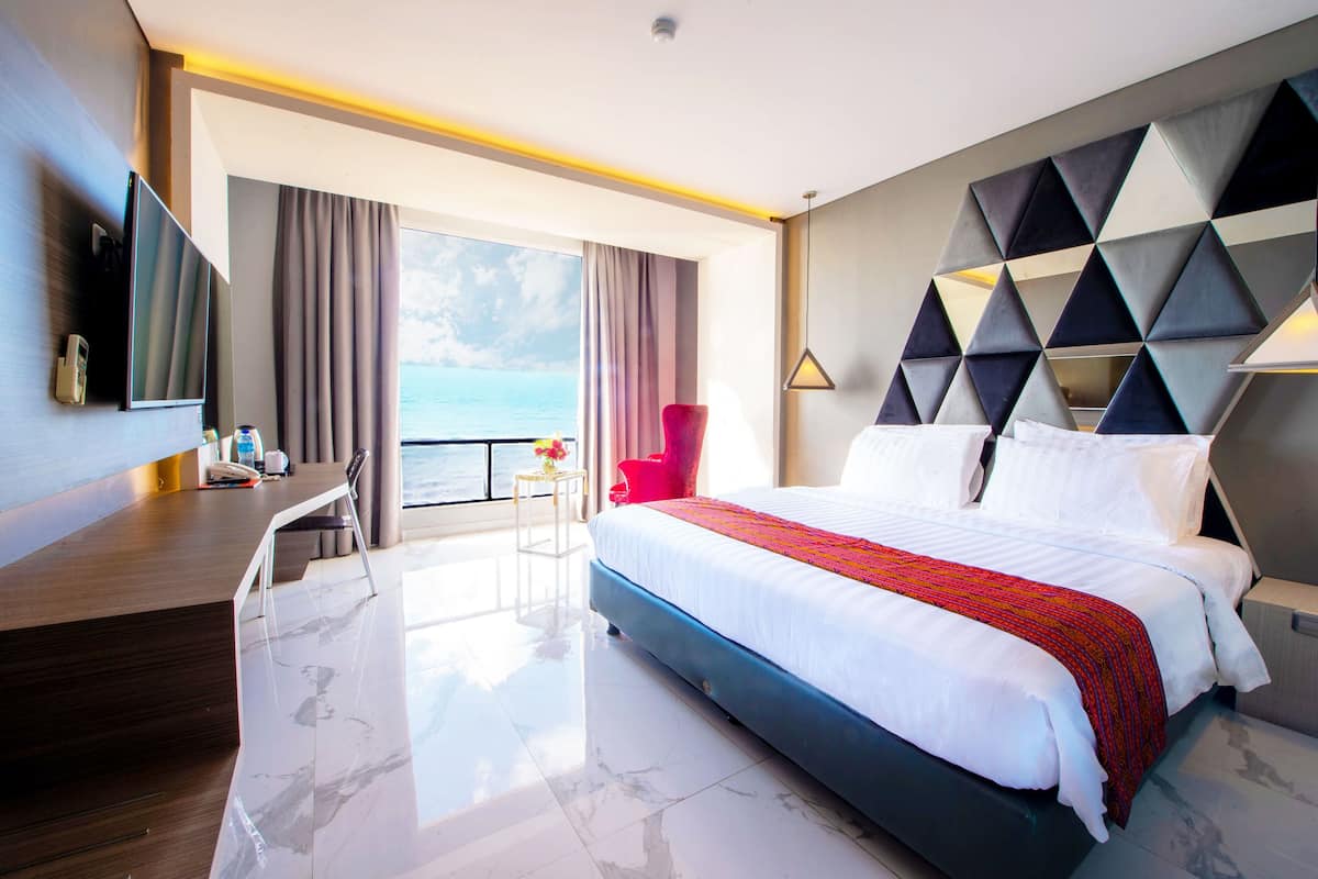 Une chambre d’hôtel avec un lit, un bureau, une chaise, une télévision et une vue sur la mer.