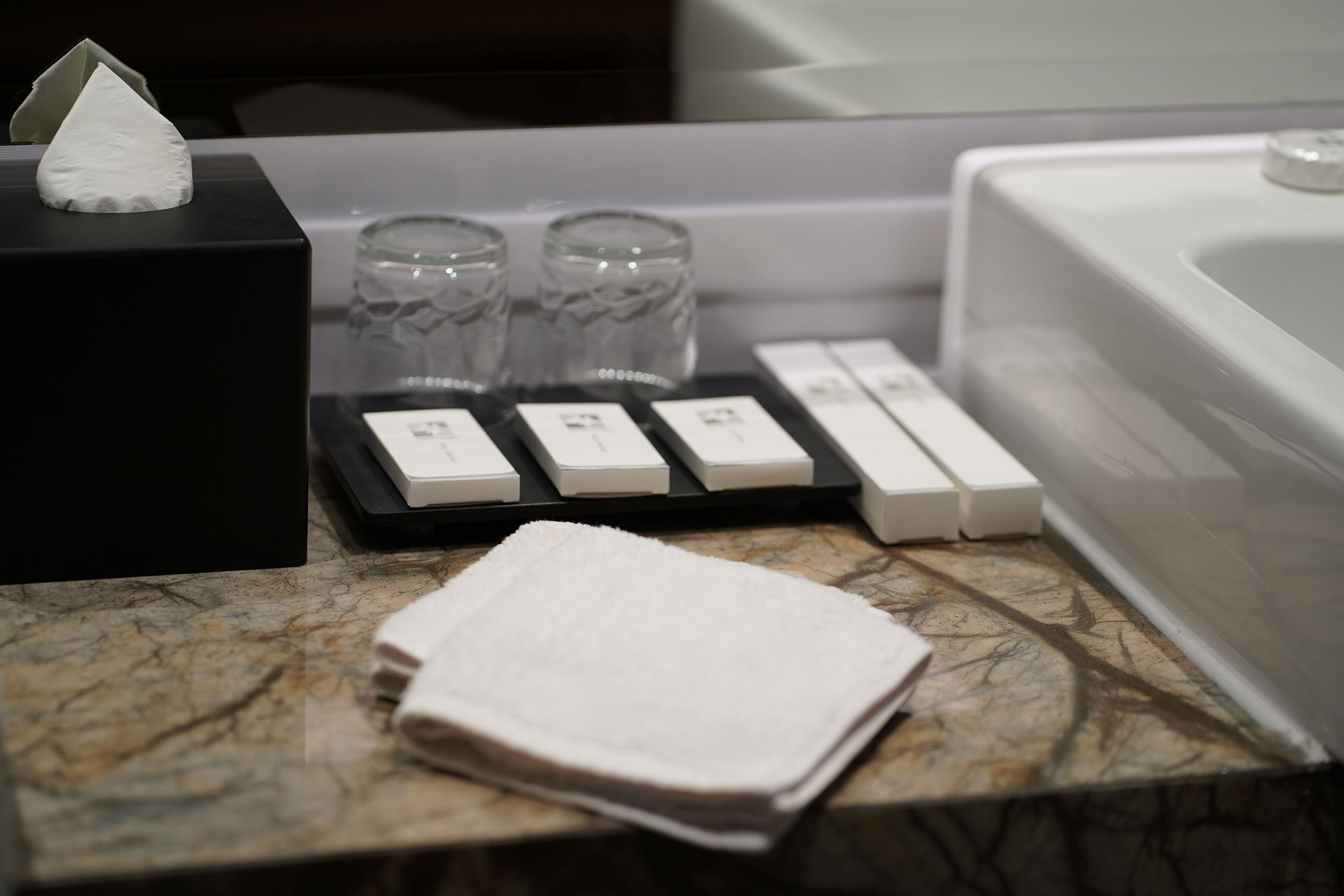 A bathroom counter with a folded towel, two glass tumblers, and a set of toiletries.