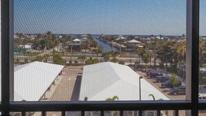 A view of a parking lot with multiple cars, a building with a white roof, and a body of water in the background.