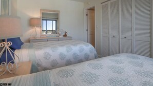 A bedroom with a bed, bedside table, lamp, dresser, mirror, and a closet.