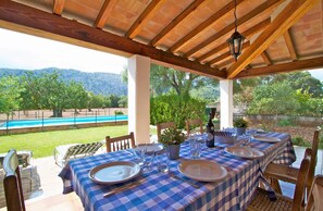 Un espace de restauration en plein air avec des nappes à carreaux, des chaises en bois et une vue sur une piscine et des montagnes.