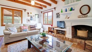 A living room with a sofa, coffee table, fireplace, TV, and bookshelves. - Finca Can Pontico - Four Bedroom House, Sleeps 6 (Pollensa)