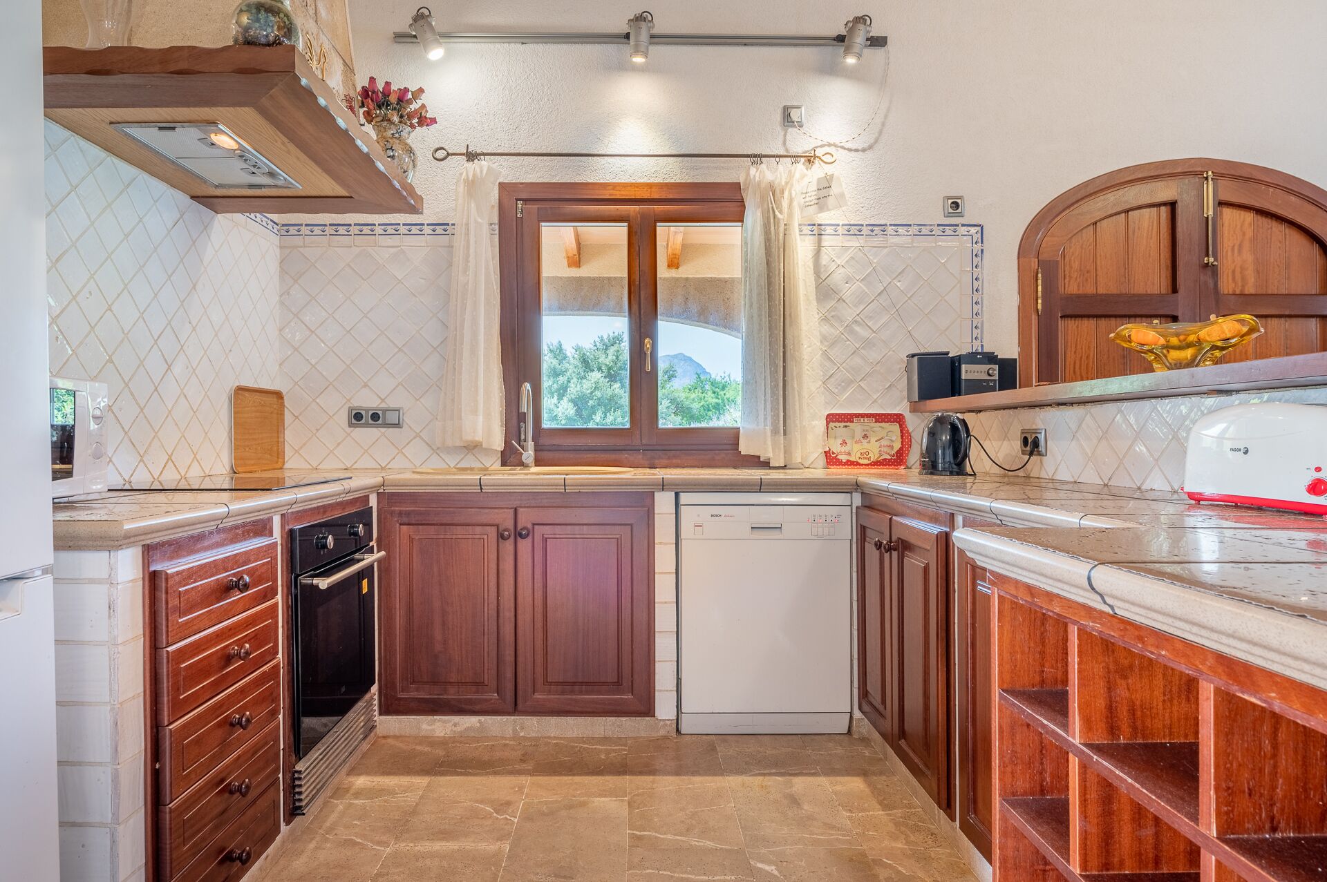 A kitchen with wooden cabinets, a dishwasher, a microwave, and a window with a view of greenery.