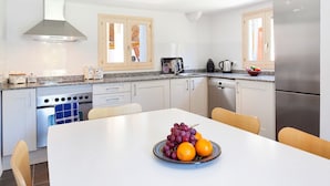 A modern kitchen with white cabinets, stainless steel appliances, and a dining area with a table set for two. - Casa Pont Roma, Private Pool, walk to restaurants (Pollença)