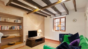 A cozy living room with a wooden TV stand, a bookshelf, and a green sofa. - Casa Pont Roma, Private Pool, walk to restaurants (Pollença)