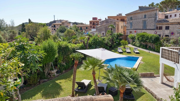 A pool area with lounge chairs and a pergola, surrounded by greenery and stone buildings. - Casa Pont Roma, Private Pool, walk to restaurants (Pollença)