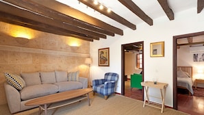 A cozy living room with a sofa, armchair, and coffee table, wooden beams on the ceiling, and a stone wall. - Casa Pont Roma, Private Pool, walk to restaurants (Pollença)