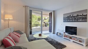 Un soggiorno moderno con un divano, un tavolino, una TV su un mobile e un balcone con vista sul verde.