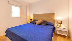 Une chambre à coucher avec un grand lit, une table de chevet, une lampe et une fenêtre.