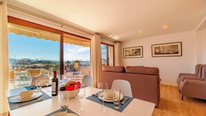 Un coin repas avec une table dressée pour deux personnes, un canapé et un balcon offrant une vue sur le port de plaisance.