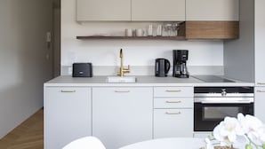 A modern kitchen with white cabinets, gold handles, a coffee maker, and a built-in oven. - 2ndhomes Ullanlinna Penthouse Apartments 2 (Helsinki)