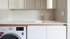 A compact laundry area with a washing machine, a sink, and a mirror above the countertop. - 2ndhomes Ullanlinna Penthouse Apartments 2 (Helsinki)