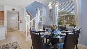 A dining area with a round table set for six, a staircase, and a view of the outdoors. - The Majorca at Windsor Westside (Kissimmee)