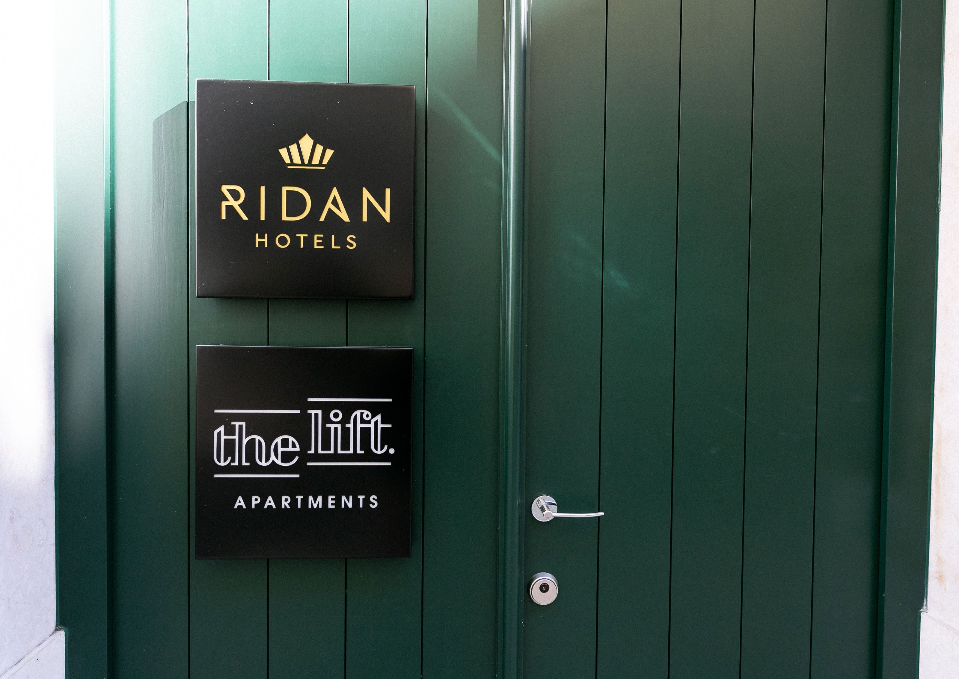 Dos carteles en una puerta verde: "RIDAN HOTELS" y "ascensor. APARTAMENTOS".