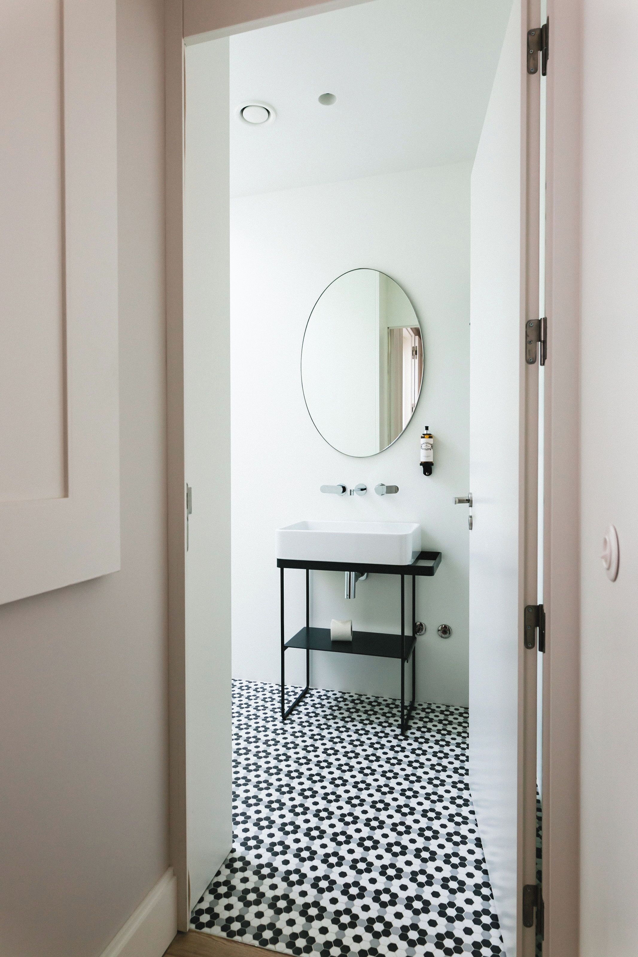 Un bagno con lavandino bianco, piano di lavoro nero e specchio rotondo. Il pavimento presenta un motivo a pois bianchi e neri.