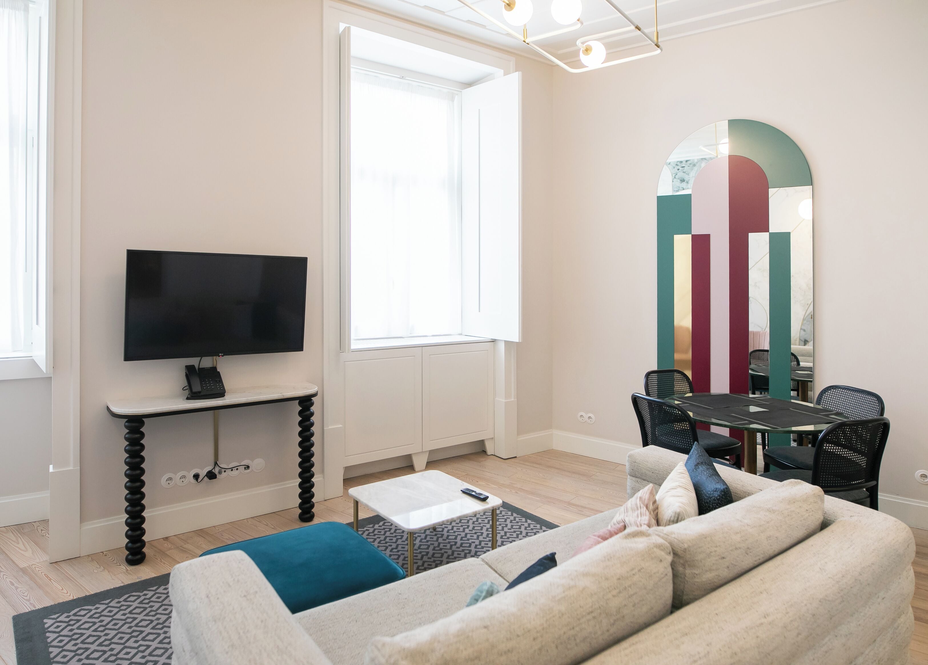 A modern living room with a flat-screen TV, a dining table with chairs, a sofa, and a large mirror on the wall.