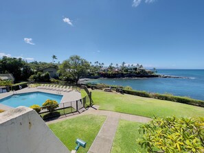 A pool area with a view of the ocean and a grassy lawn.