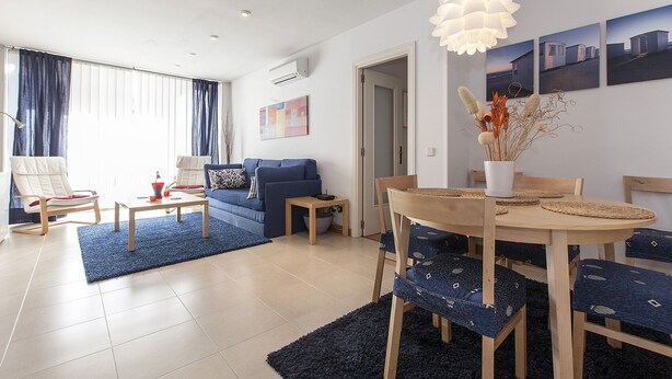 Una sala de estar moderna con un sofá azul, una mesa de comedor de madera con sillas azules y una lámpara colgante.