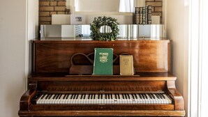 Um piano de cauda imponente com um banquinho de pele, um espelho acima e uma parede de tijolos ao fundo.