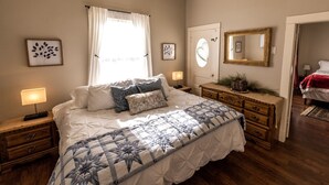 Quarto com cama grande, abajures, cômoda, espelho e obras de arte nas paredes.