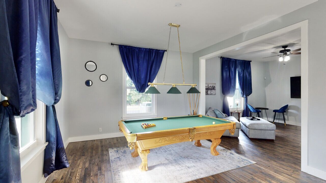 A pool table in a room with a wooden floor, blue curtains, and a ceiling fan.