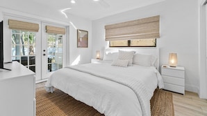 Une chambre avec un grand lit, des murs blancs, un ventilateur de plafond et une vue à travers les portes vitrées.