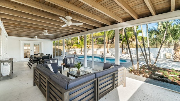 Une terrasse extérieure avec une piscine, des poutres en bois au plafond et un espace détente avec une table et des chaises.