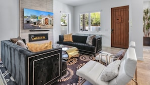 Una sala de estar moderna con chimenea, sofás blancos y negros y un televisor grande.