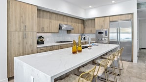 Una cocina moderna con una isla grande, armarios de madera, electrodomésticos de acero inoxidable y sillas tipo bar.
