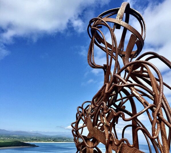 A complex metal sculpture against a clear blue sky with a distant landscape. - Boutique-style holiday cottage, beautifully decorated with wood burner & hot tub (Llanbedrog)