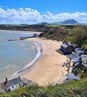 A coastal beach with a stone building and a mountain in the background. - Boutique-style holiday cottage, beautifully decorated with wood burner & hot tub (Llanbedrog)