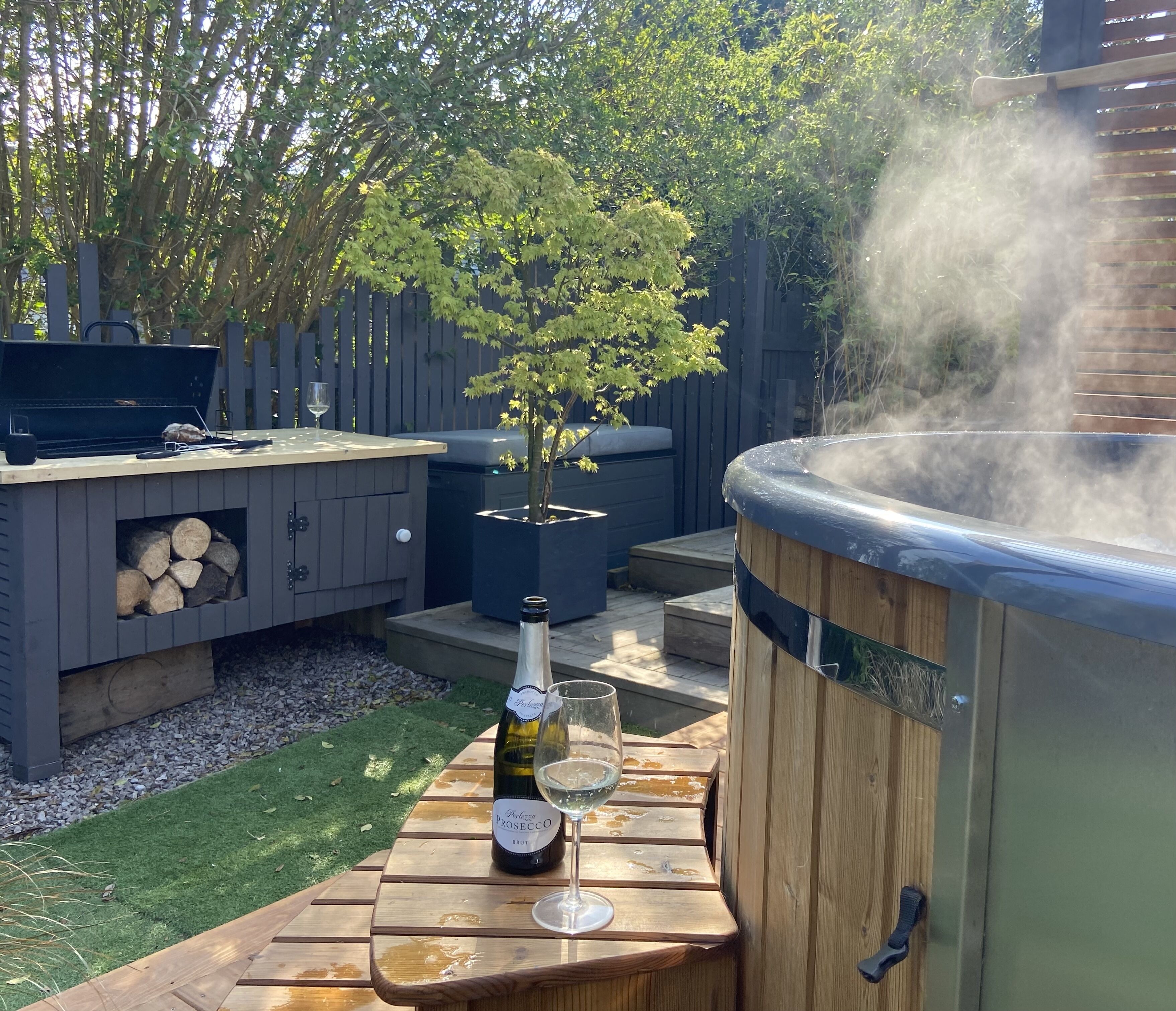 An outdoor patio with a hot tub, a grill, and a bottle of Prosecco.