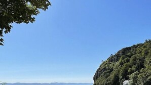 Een strand met een rotsachtig pad dat naar het strand leidt, een heldere lucht en een verafgelegen uitzicht op zee en bergen.