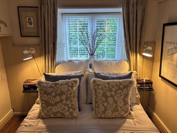 A bedroom with a bed, two bedside lamps, a window with blinds, and a framed picture on the wall. - Boutique-style holiday cottage, beautifully decorated with wood burner & hot tub (Llanbedrog)