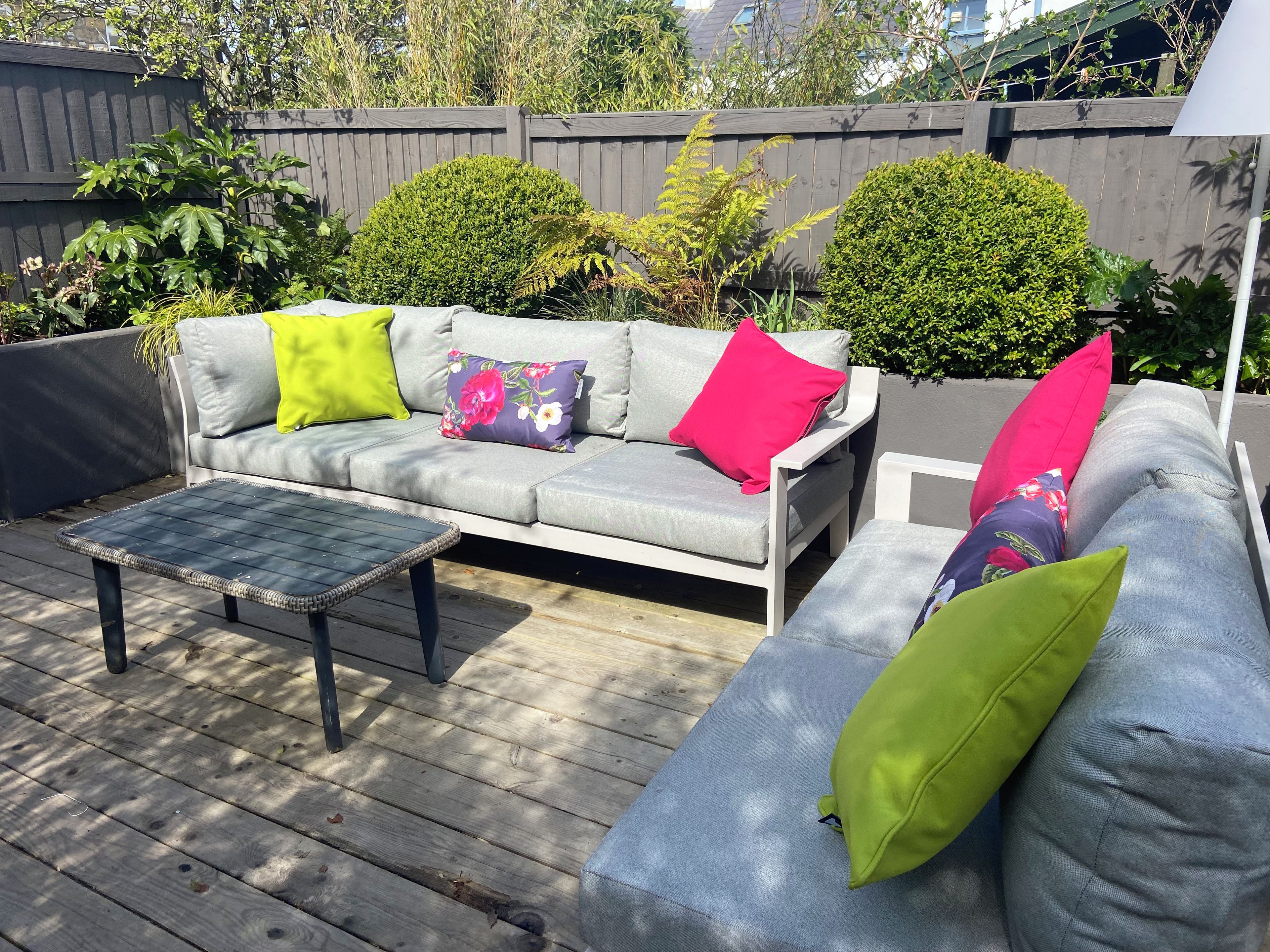An outdoor seating area with a grey sofa, a small table, and a wooden deck.