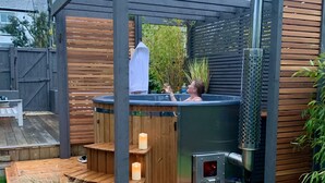 Een jacuzzi onder een houten pergola met een ingebouwde houtkachel.