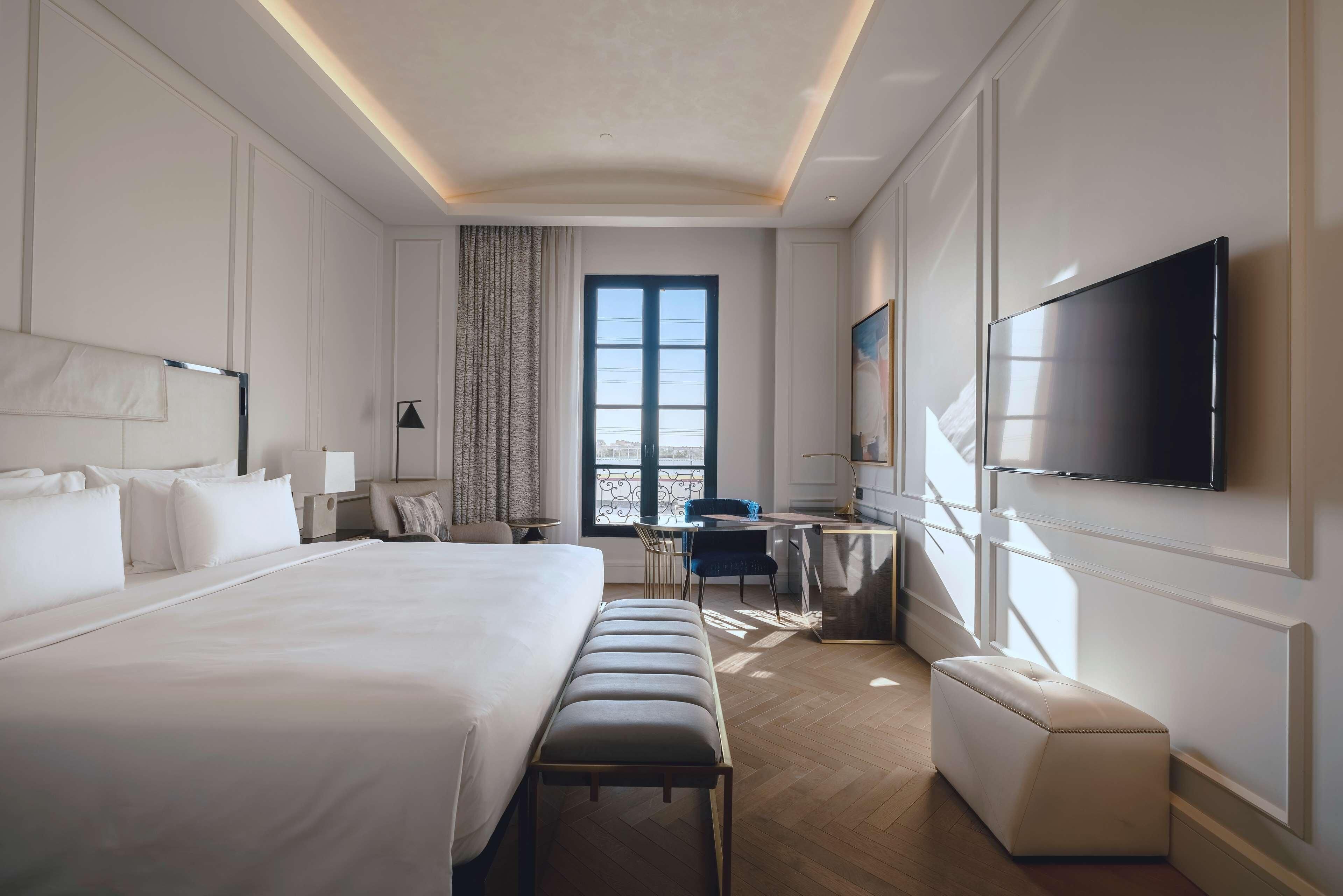 Ein Hotelzimmer mit einem großen Bett, einem Schreibtisch, einem Sessel, einem Fernseher und einem Fenster.