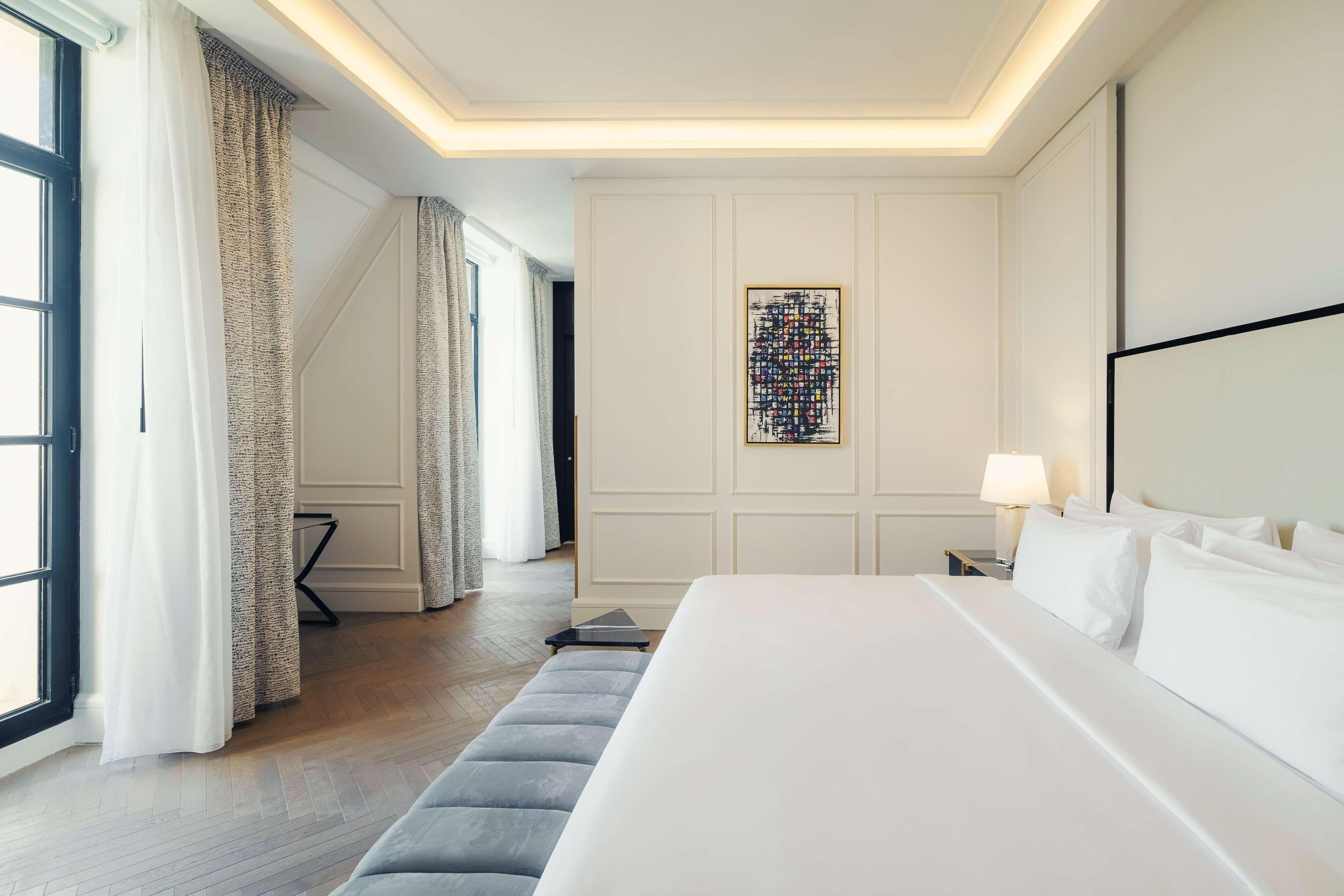 Ein Hotelzimmer mit einem großen Bett, einem Schreibtisch mit Lampe, einem Bild an der Wand und einem fenster mit Vorhängen.