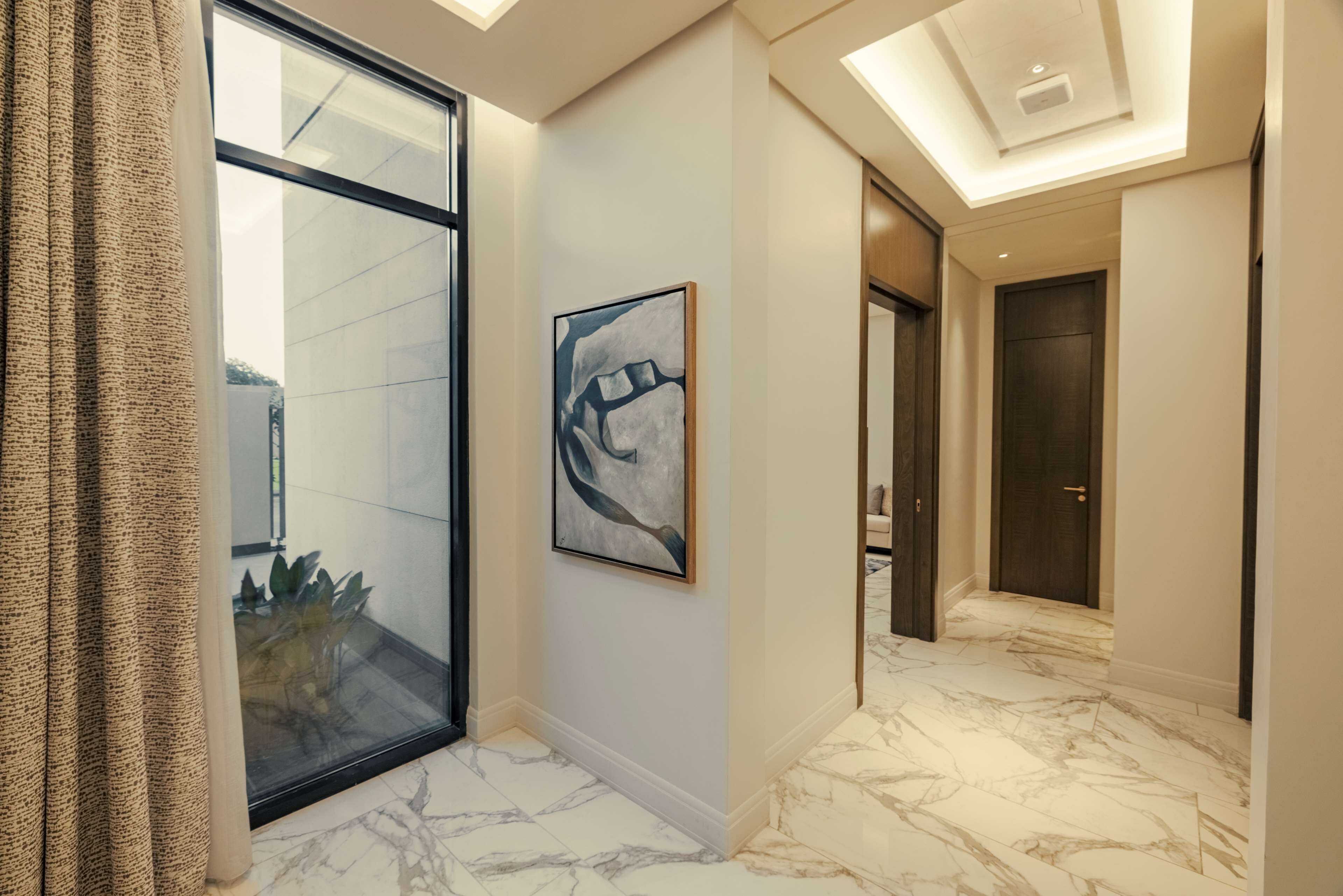 A hallway with a glass door, a marble floor, and a framed abstract painting.