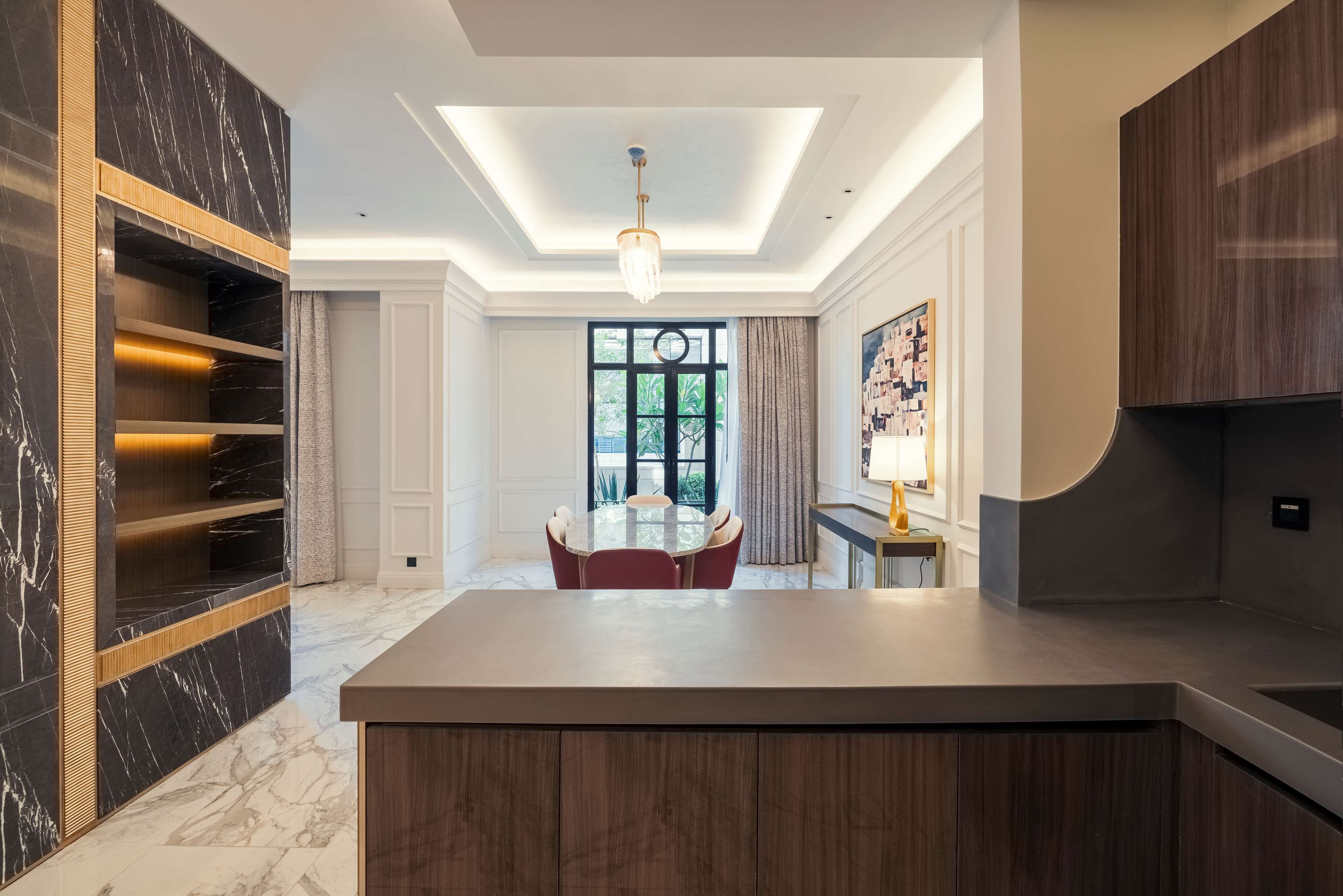 A modern kitchen with a central island, built-in shelving, and a dining area with a round table and chairs.