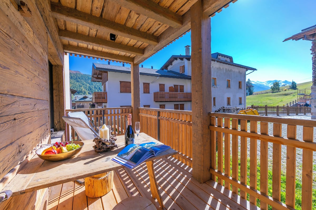 A wooden deck with a table, a bowl of fruit, a bottle, and a magazine.