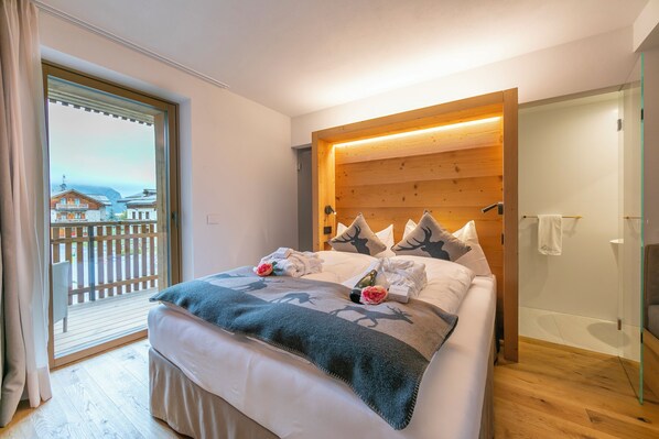 A hotel room with a bed, a wooden headboard, a view of a balcony, and a shower area.